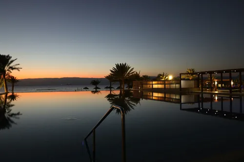Piscina de borda infinita refletindo palmeiras ao entardecer